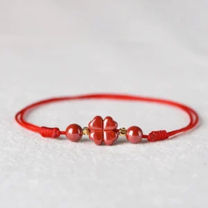 Four leaf clover cinnabar red string bracelet with gold spacer beads on light grey background