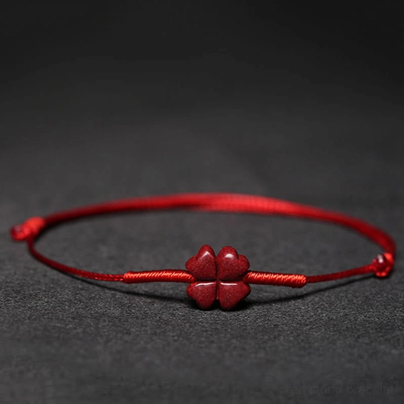Red blessing bracelet with four-leaf clover on black display stand