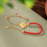 Gold-plated four-leaf clover red string bracelet with adjustable chain on vintage calligraphy book