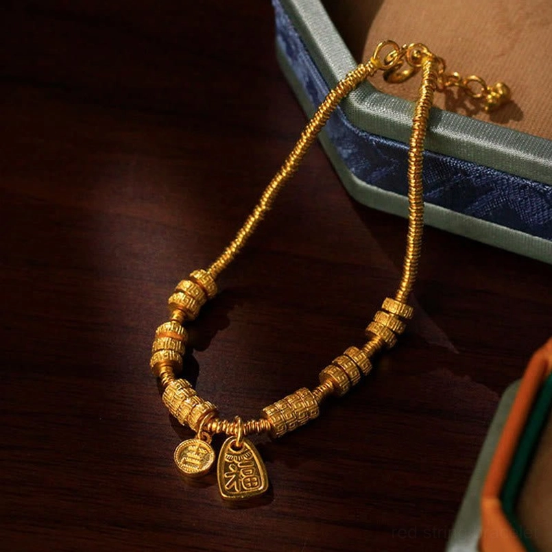 Vintage-style gold Fu character bracelet with carved barrel beads and dual pendants on wooden surface