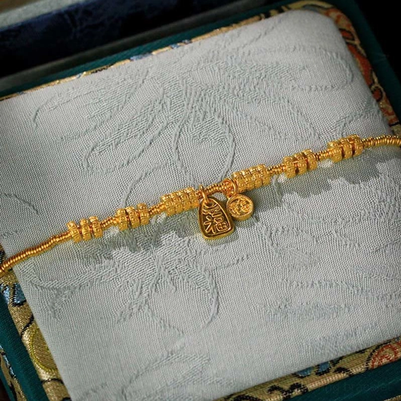 Side oblique view of handcrafted gold Fu bracelet with decorative spacer beads on jewelry box