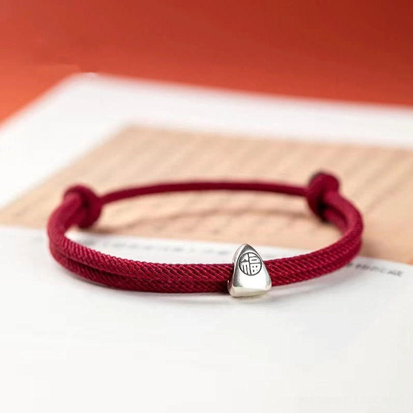 Sterling silver fu charm red string bracelet placed on book lifestyle photo
