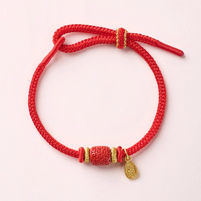 Red string fu character bracelet with engraved copper bead and gold details on light background
