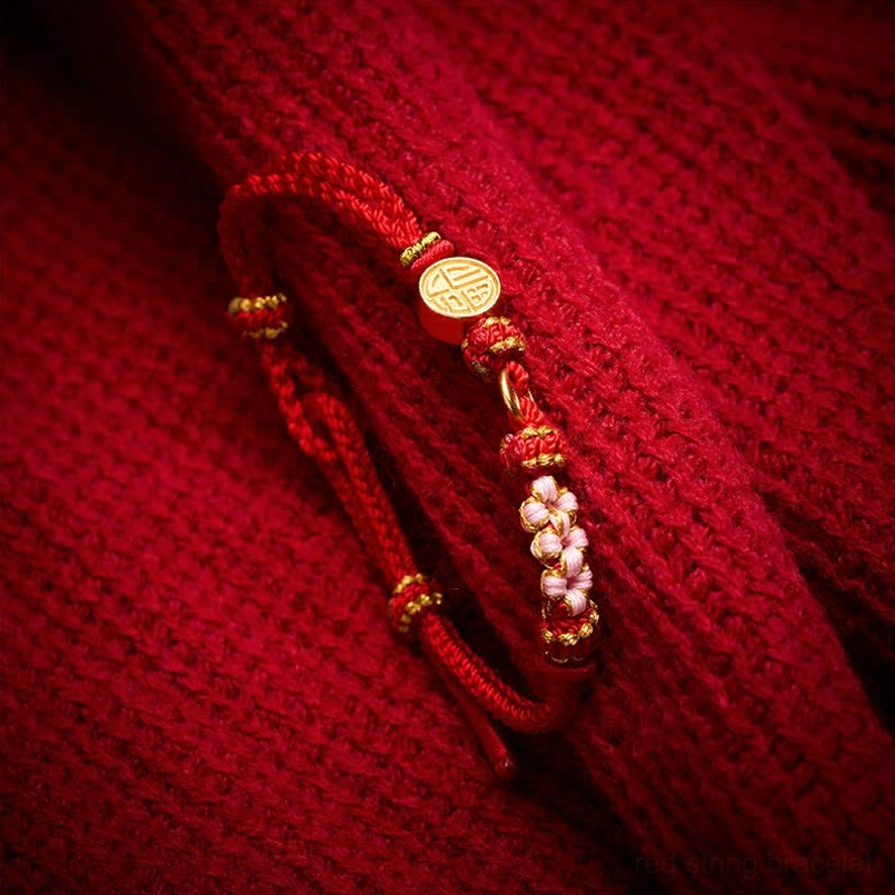 Close up view of gold Fu charm red braided string bracelet with flower beads