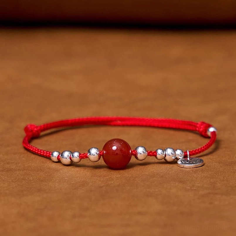 Red agate fortune bracelet with silver Fu pendant and beads on wooden surface