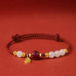 Fu character jade cinnabar red string bracelet with gold charm, side flat lay view on red background