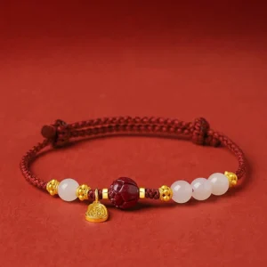 Fu character jade cinnabar red string bracelet with gold charm, side flat lay view on red background