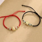 Fu character jade bead red string bracelet flat lay top view with gold charm and woven cord
