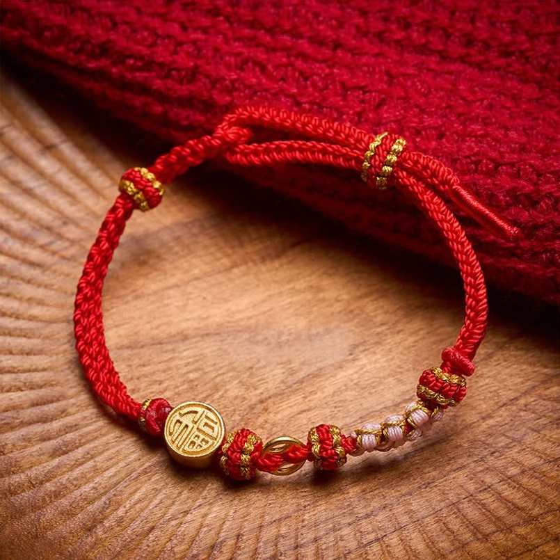 Fu charm red string bracelet flat lay on wooden board with red knitted fabric
