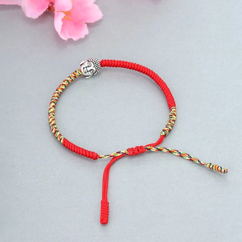 Full red woven serenity Buddha string bracelet on light gray background with pink flower