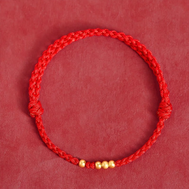 Full top view of double knot red string gold bead bracelet on red flat background