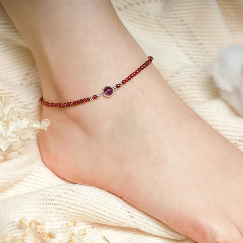 Burgundy red beaded anklet with purple gem worn on ankle close-up