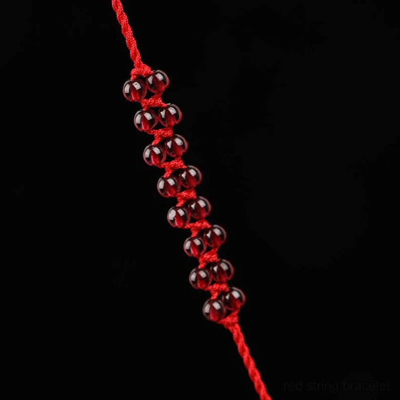 Close-up detail of deep red garnet beads and braided red string belly chain on black background