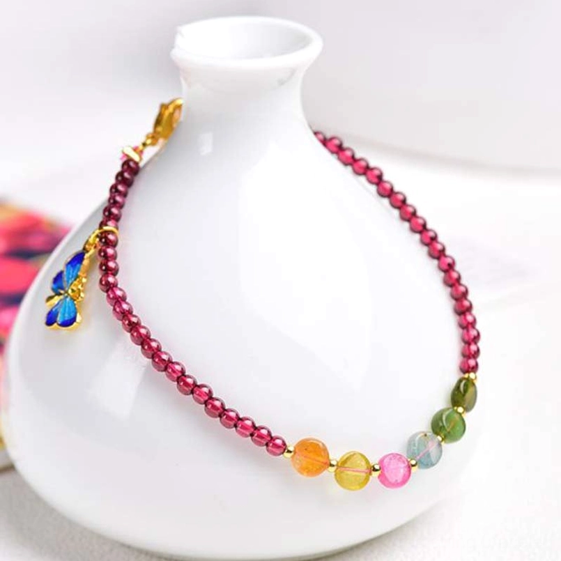 Garnet tourmaline ankle bracelet displayed on ceramic vase with floral backdrop
