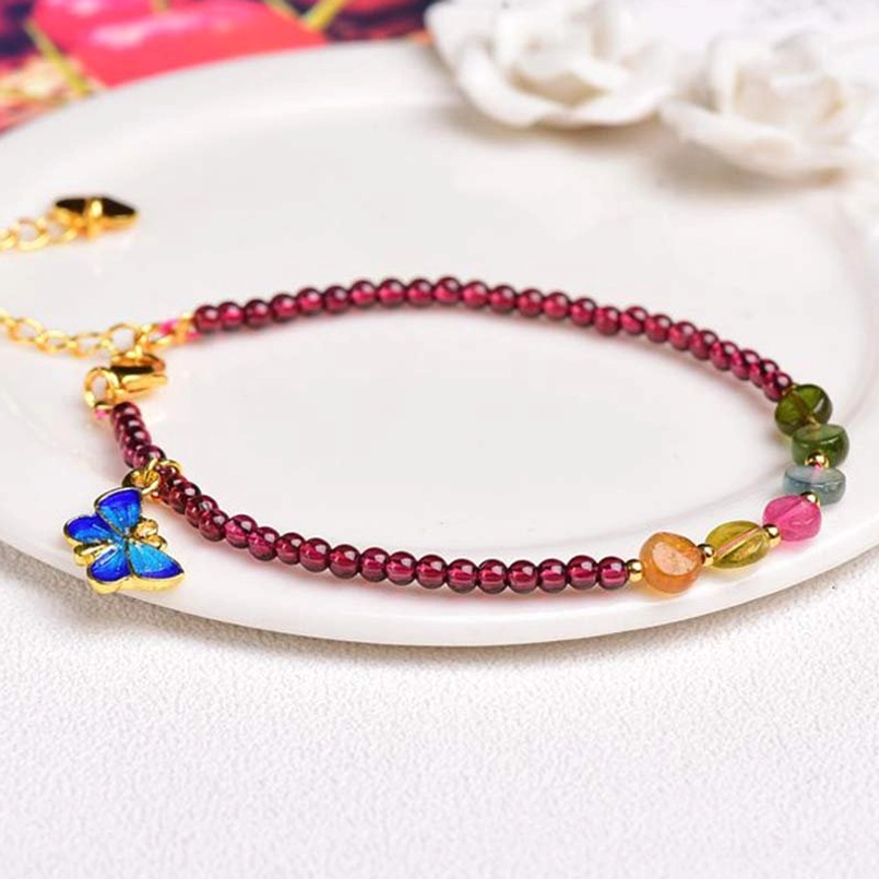Garnet tourmaline butterfly charm bracelet flatlay with white flowers and gold hardware