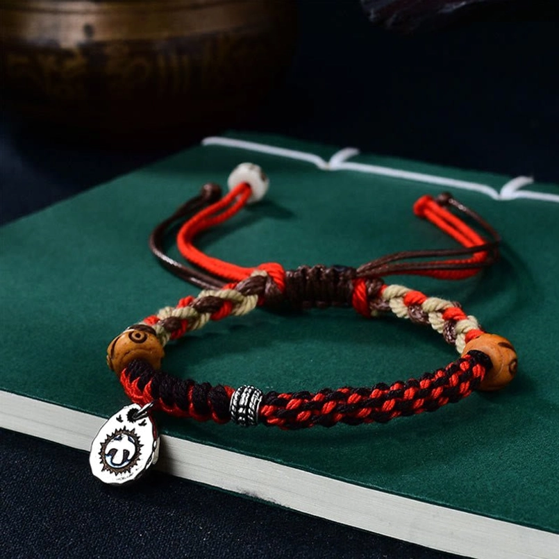 Red and brown woven Garuda bracelet with adjustable knot design and wooden beads on book background