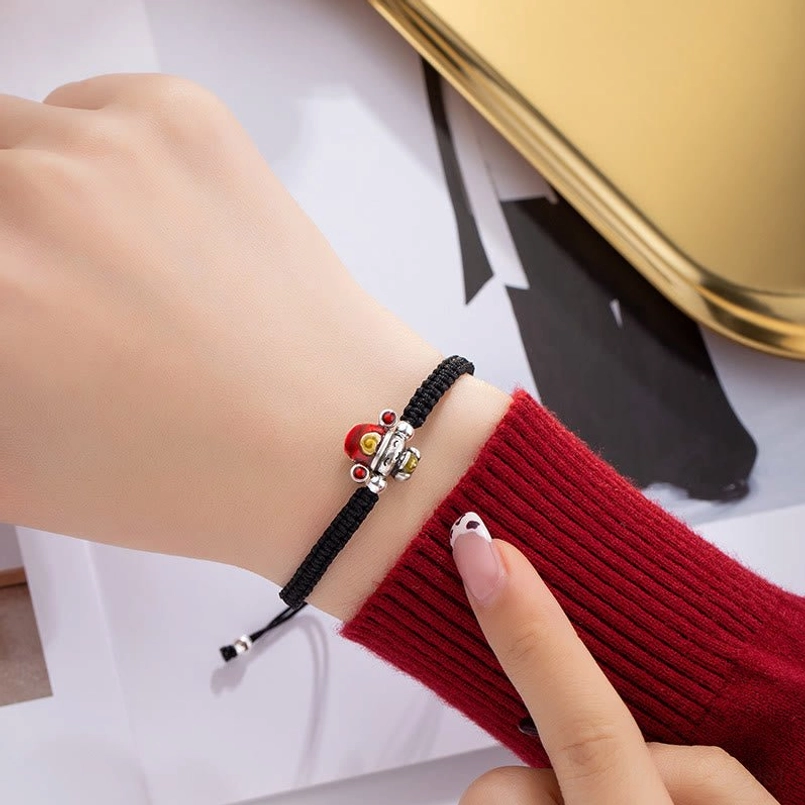 Black God of Wealth bracelet worn on wrist with red knit sleeve in minimalist office background
