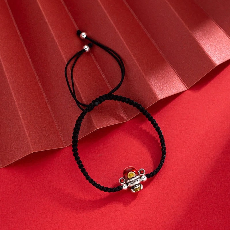 Black woven God of Wealth bracelet with silver fortune charm and adjustable pull knot on red folded paper