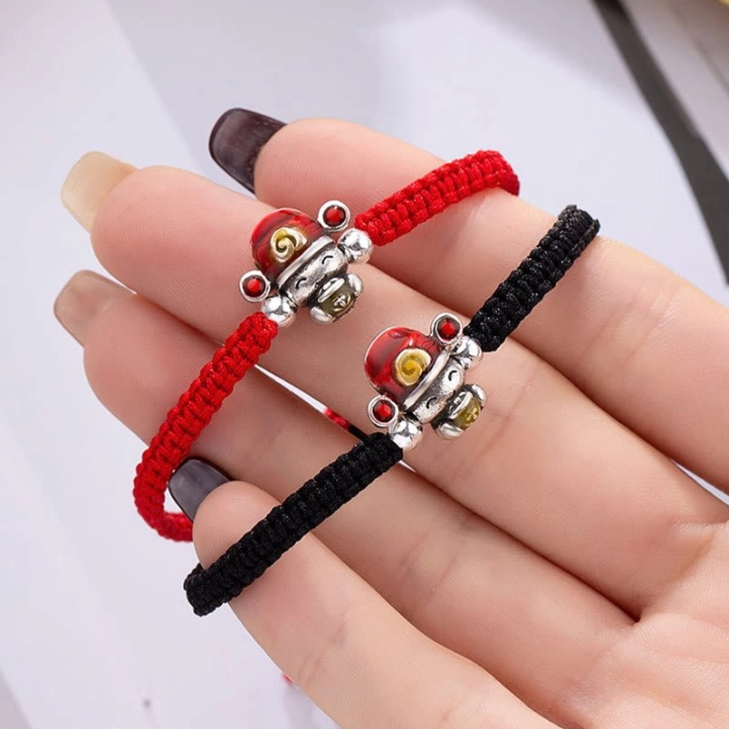 Hand-held close-up of red and black God of Wealth woven bracelets showing detailed silver fortune charms