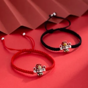 God of Wealth red and black woven string bracelets with silver fortune charms displayed on red folded paper backdrop