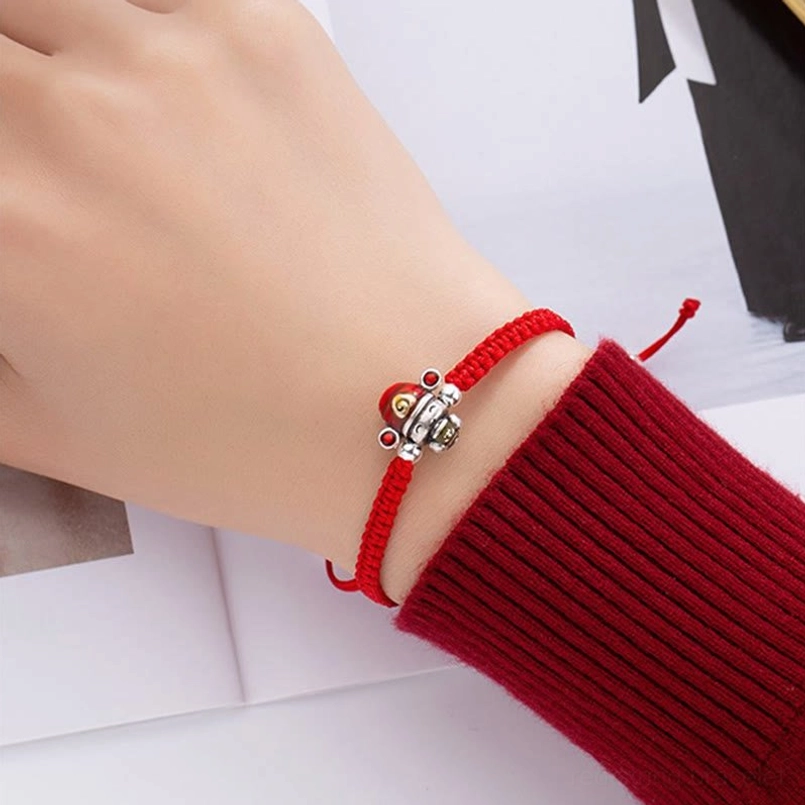 Close-up side view of red woven God of Wealth bracelet with detailed silver fortune charm on white background
