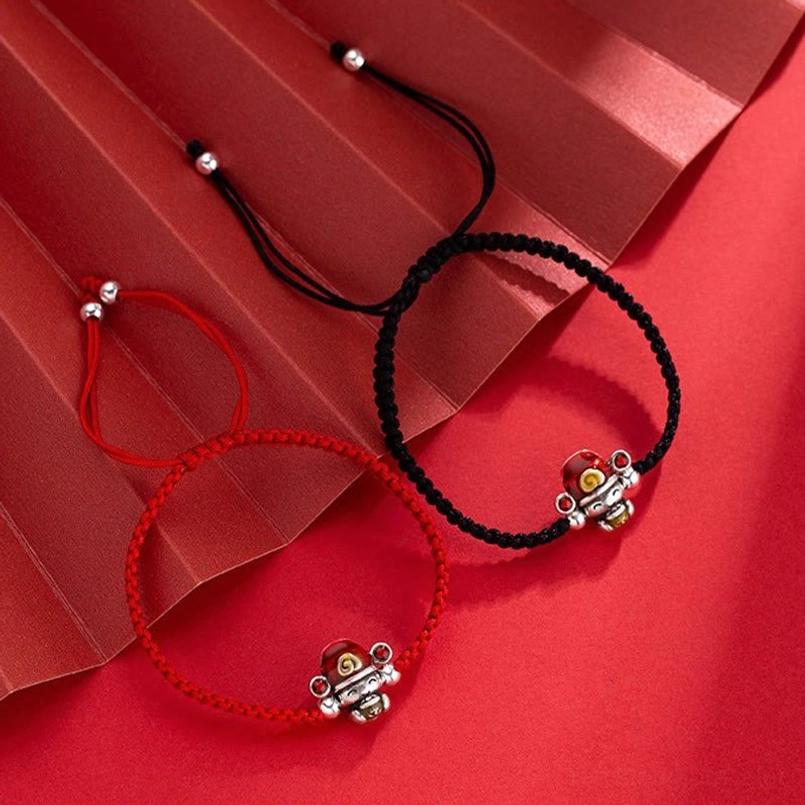 Pair of handmade God of Wealth bracelets in red and black cord with matching silver fortune charms on textured red background