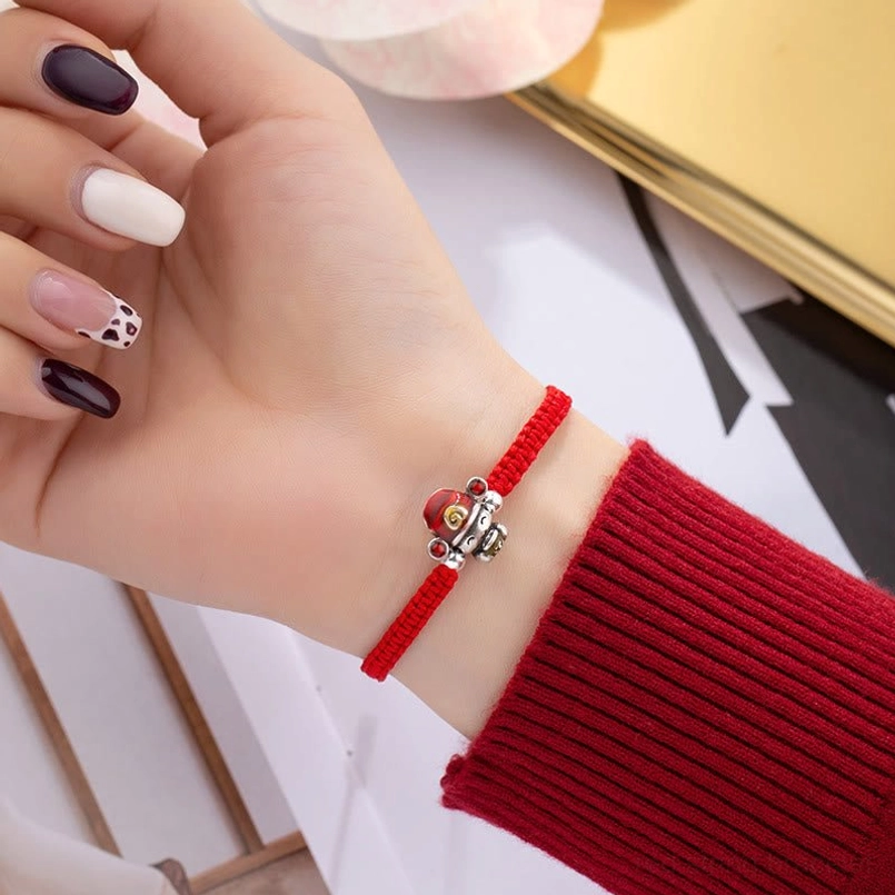 Red God of Wealth bracelet worn on wrist with red knit sleeve in minimalist desk setting
