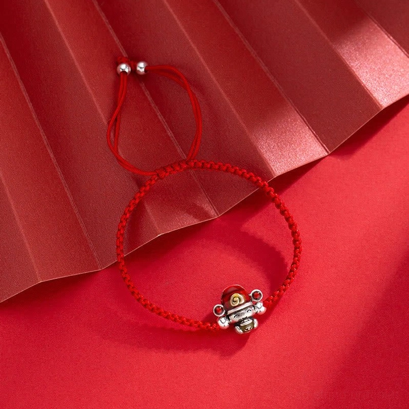 Single red God of Wealth bracelet with woven cord and silver fortune charm on pure red paper background