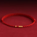 999 gold beads red string couple bracelet with adjustable knot, three-quarter view showing five matte gold beads on burgundy backdrop