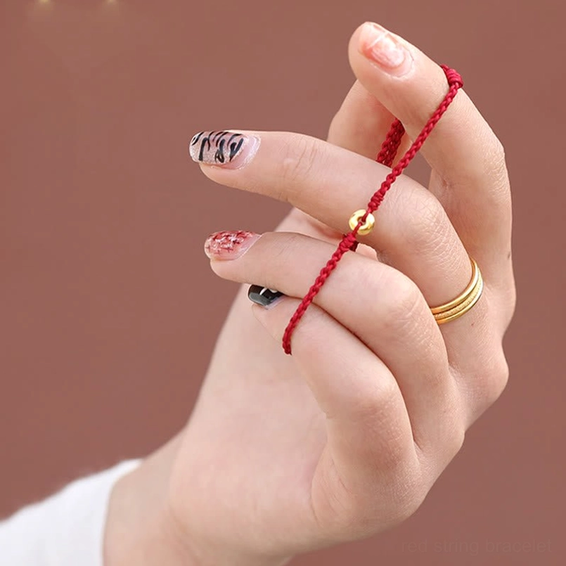 red string bracelet with gold peace buckle held in hand close-up detail