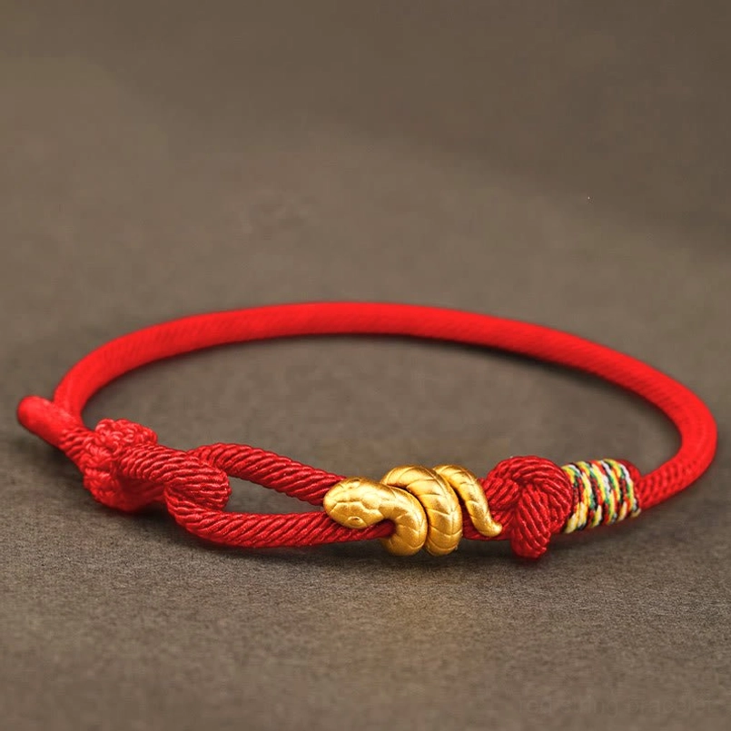 gold snake red string bracelet flat lay on textured fabric background