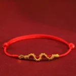 999 gold snake red string braided bracelet with wavy gold weave and metal beads on dark background