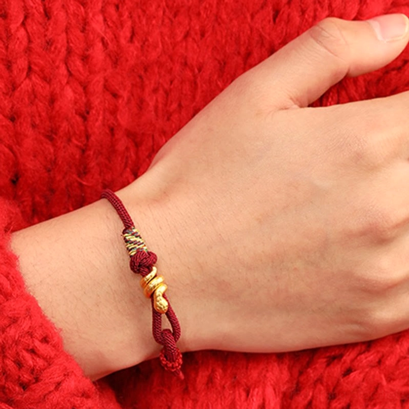 gold snake red string bracelet worn on left wrist close up with red sweater background