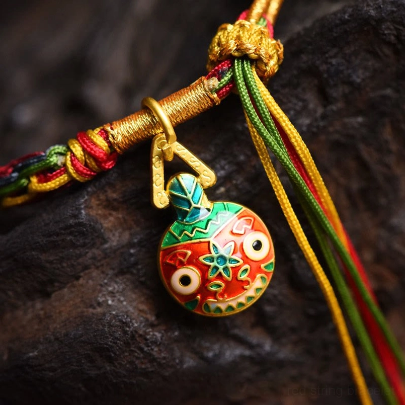 Close up of Gold Swallowing Beast enamel charm on braided bracelet