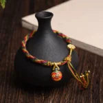Gold Swallowing Beast Mother multicolor braided luck bracelet with gold hardware and enamel charm on dark wooden table