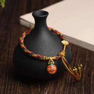 Gold Swallowing Beast Mother multicolor braided luck bracelet with gold hardware and enamel charm on dark wooden table