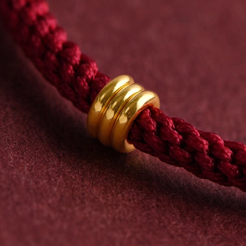 Close-up macro view of 999 gold triple ring charm on red braided rope