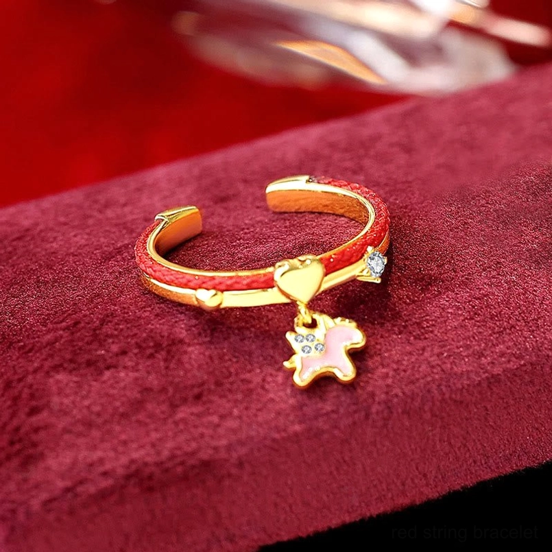 Gold-toned unicorn charm red string open ring with heart accent on burgundy velvet display