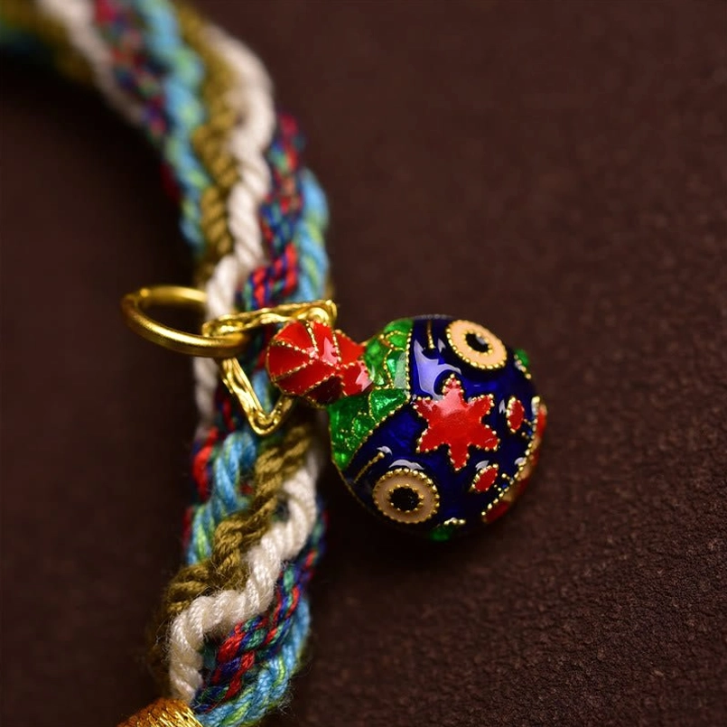 Macro close up of cloisonne Swallowing Beast charm on woven red string bracelet