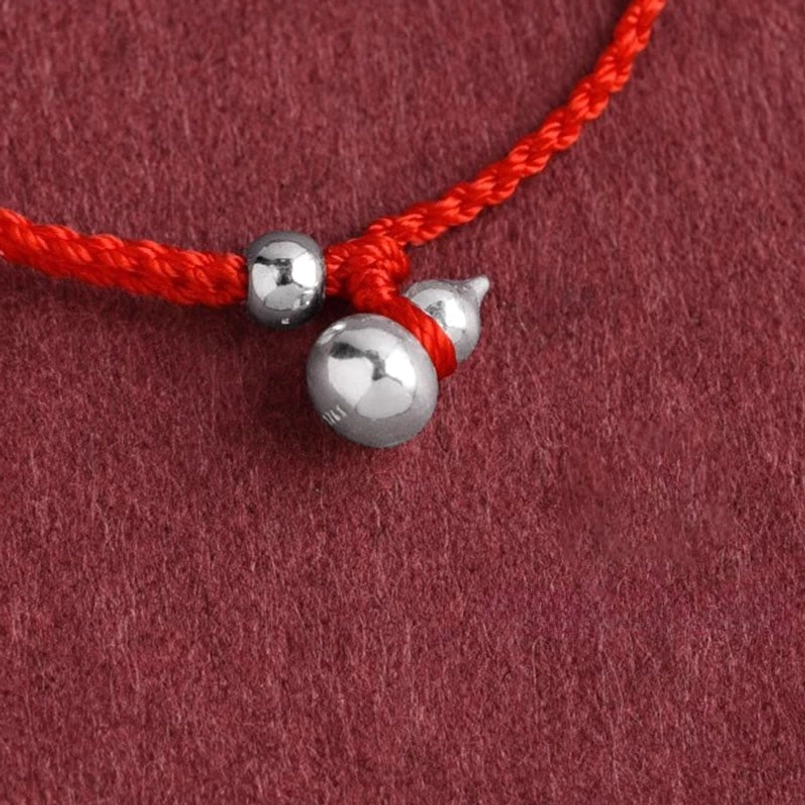 silver gourd charm tied to red string bracelet connection detail