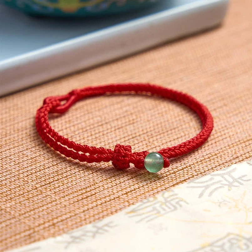 Green aventurine red string bracelet with fixed knot on printed calligraphy paper and woven mat