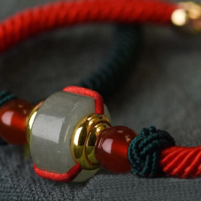 Macro detail view of green aventurine barrel bead, gold metal parts, and red agate beads on braided cord