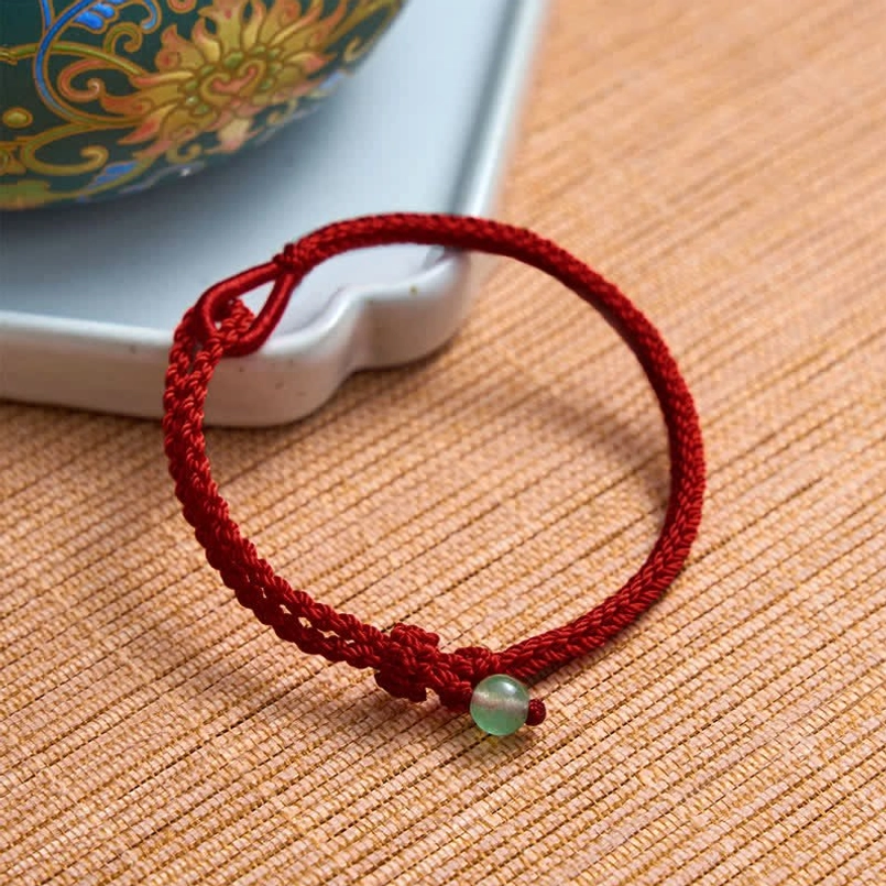 Green aventurine red string bracelet with decorative knot on ceramic tray and woven mat