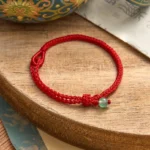 Green aventurine red string balance bracelet on wooden table with oriental decor and decorative knot detail