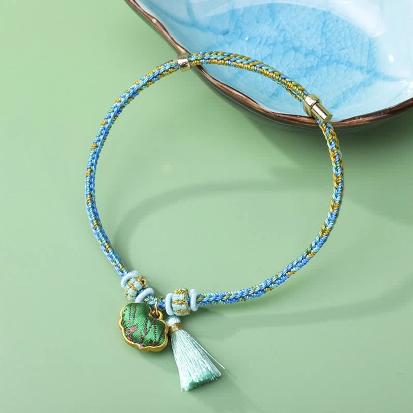 Green five-color braided cord luck bracelet with enamel charm and green tassel on ceramic plate