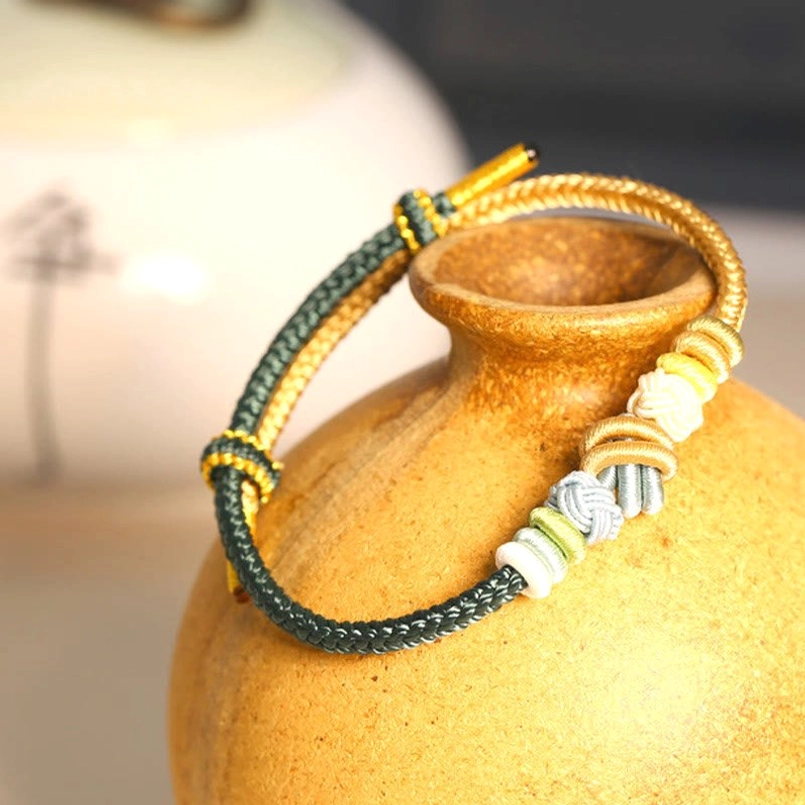Dark green and gold two-tone peace knot bracelet displayed with ceramic vase retro delicate woven design