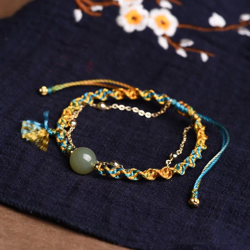 Green jade prosperity bracelet with blue and yellow braided cord on dark background