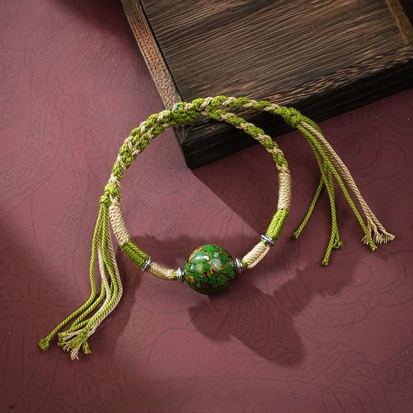 Green lacquer craft braided red string bracelet with tassel on dark red background