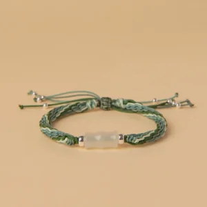 Green and white jade bamboo reincarnation knot red string bracelet with silver tassel beads, top-down view