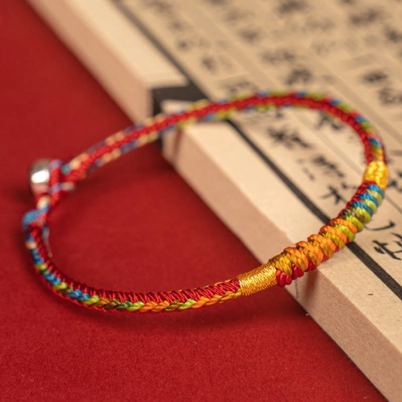 Hand braided lucky red string bracelet with silver bell clasp on ancient Chinese book background